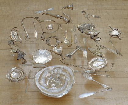 Squashed silverware arranged to lay flat in a pool, suspended just above the ground.