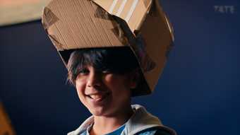 A boy wears a cardboard hat on his head