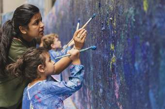 A child and adult painting onto a blue wall with paintbrushes