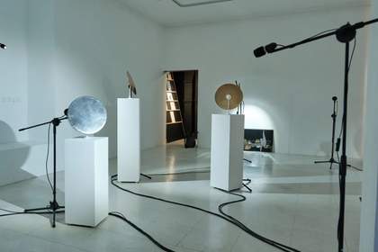 A white gallery featuring three installations of metal pans on pedestals and black cord on the floor