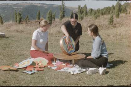 Three women sitting on a field outside where one of them is spinning a metal pan.