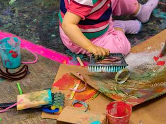 a child holds a scrubbing brush and paints with it on cardboard