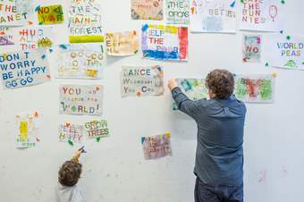 A person and a child attaching colourful banners to a wall