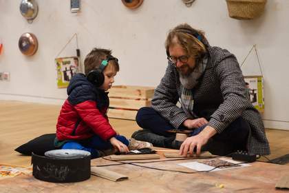 A man and a boy wearing headphones look at something on the floor