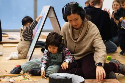 A woman and a boy sit together to look at something on the floor with headphones on