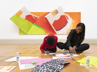 An adult and a child sitting on the floor in an art gallery drawing with art materials