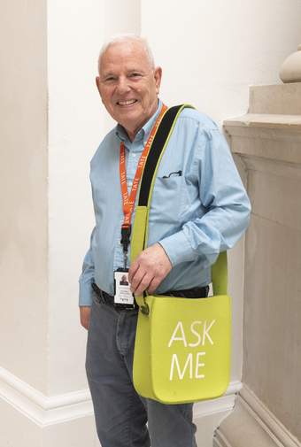 A person wearing a Tate staff lanyard smiling with a colourful bag that says 'Ask Me'