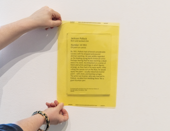 A person holding a yellow overlay over wall text