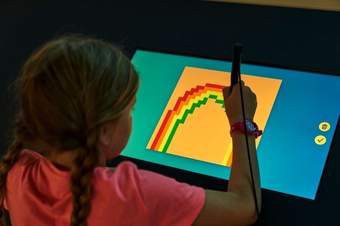A young girl drawing a rainbow on a screen.