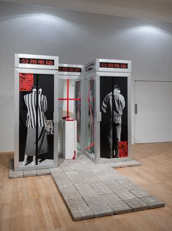Dialogue is an installation that comprises two life-size aluminium alloy telephone booths, a mirror, a pedestal, a red telephone and cement paving stones.