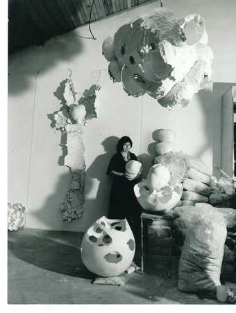 An archival photography of a woman standing between egg-like and nature-inspired sculptures
