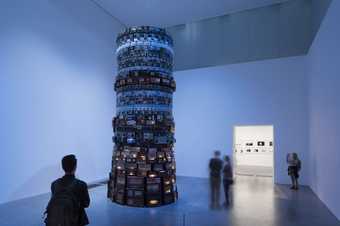 A group of people looking at a cylindrical tower of televisions