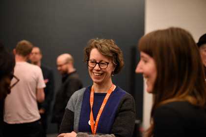 Three people talk and smile, others are gathered in another small group in the background