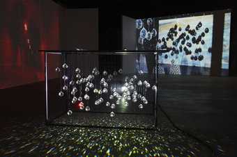 A metal construction hung with crystals, their shadows projected onto a screen behind