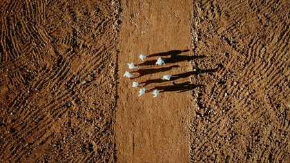 An aerial image of people wearing white outfits, walking in a circle in a field