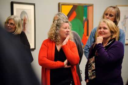 A group of people standing in a gallery room with paintings behind them, mouths open in conversation.