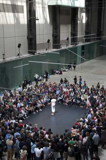 A male dancer dressed in white stands in front of a crowd who have formed a square around the stage