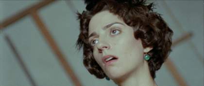 A film still showing a woman with short brown curly hair staring to the left