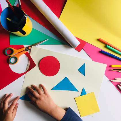 a pair of children's hands moving collage shapes around, red circle blue triangles and yellow square