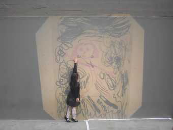 Image shows a young girl stood in front of a projection. She stands on tip toes and reaches her hand up to touch the wall.
