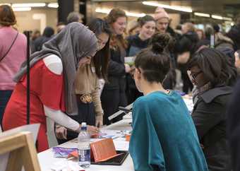 A group of young people lean across a stand, talking and looking at printed material, at the Alternative Careers Fair