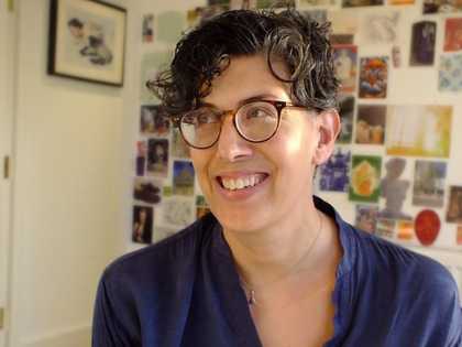 Head-and-shoulders photo of a person smiling, eyes looking away from the camera towards upper left; behind is a wall covered in postcards and images