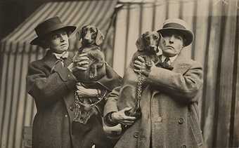 Two women in over sized tweed suits carrying their dogs