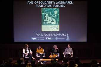 Four people onstage in the auditorium at Tate Modern, sitting in front of a projected screen featuring the title of the conference, during a panel discussion