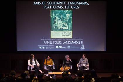 Four people onstage in the auditorium at Tate Modern, sitting in front of a projected screen featuring the title of the conference, during a panel discussion