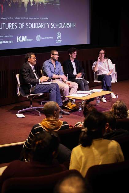 Four people sit on a panel onstage listening to an audience member during a conference Q&A