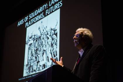 Photograph of someone speaking in front of a projected image onstage in the auditorium at Tate