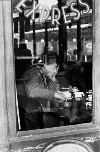A black and white photograph of Alberto Giacometti sitting in a Parisian cafe