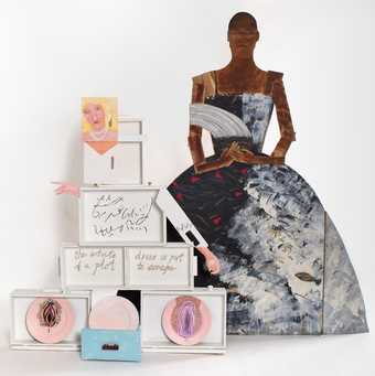 on the left, a figure with blonde hair and a pearl necklace assembled from white painted boxes; on the right, a wooden painted cut out of a person in a ball gown 