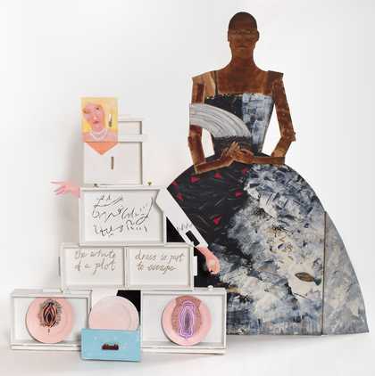 on the left, a figure with blonde hair and a pearl necklace assembled from white painted boxes; on the right, a wooden painted cut out of a person in a ball gown