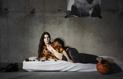 person looking directly into the camera on a mattress on the floor in a concrete room