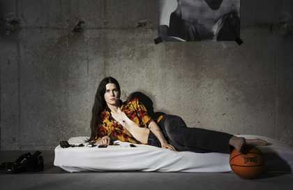 person looking directly into the camera led on a mattress on the floor in a concrete room