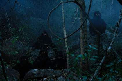 Misty dark film still of two people wearing black hooded clothing with lights for eyes in a woodland scene
