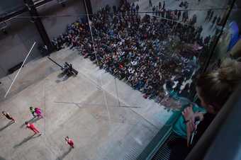 angled birds eye view of dancers standing still in pink leotards with crowd watching