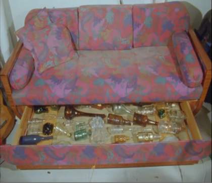 Film still showing bottles under a sofa