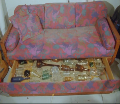 Film still showing bottles under a sofa