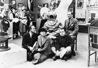 A black and white photograph of Diana Brinton-Lee, Salvador Dalí (in diving suit), Rupert Lee, Paul Éluard, Musch Éluard, ELT Mesens at the International Surrealist Exhibition in London (1936).