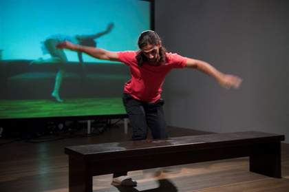 A performer in a gallery space with a projected image in the background
