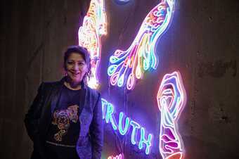 Chila Kumari Singh Burman stands in front of her neon artwork.