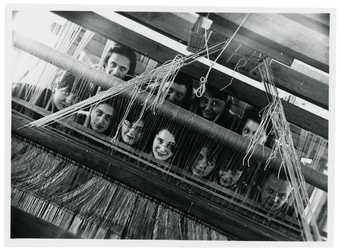 A group of Bauhaus weavers looking through the loom in to the camera