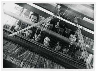 a group of female weavers looking at the camera through the loom