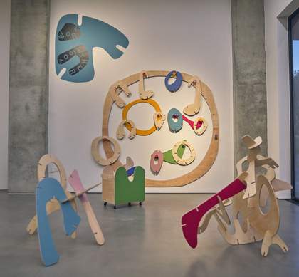 A large room filled with curved, colourful wooden sculptures. On the wall there's a blue carved shape with the words 'Work Together' painted on them.