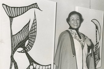 A photo of artist Huguette Caland in front of hung artwork