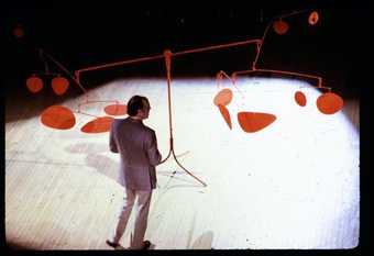 Man in a suit looks at a giant red Calder kinetic sculpture entitled Chef d’Orchestre