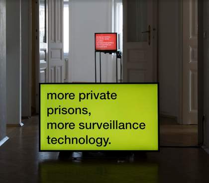 Two videos can be seen on monitors in separate rooms of a gallery, each with text on a single-coloured background