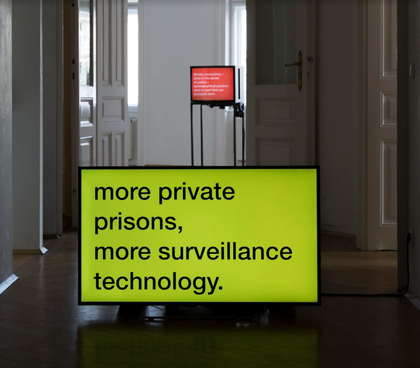 Two videos can be seen on monitors in separate rooms of a gallery, each with text on a single-coloured background